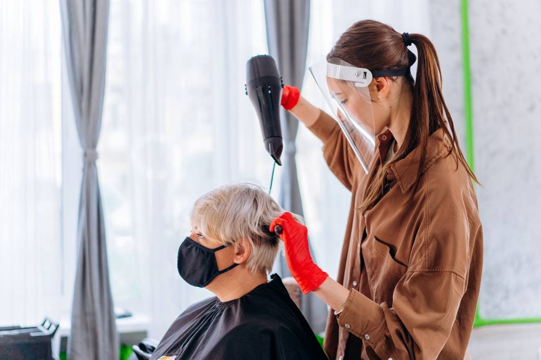 A stylist blow-dries a woman's hair using a brush and hairdryer in a salon.