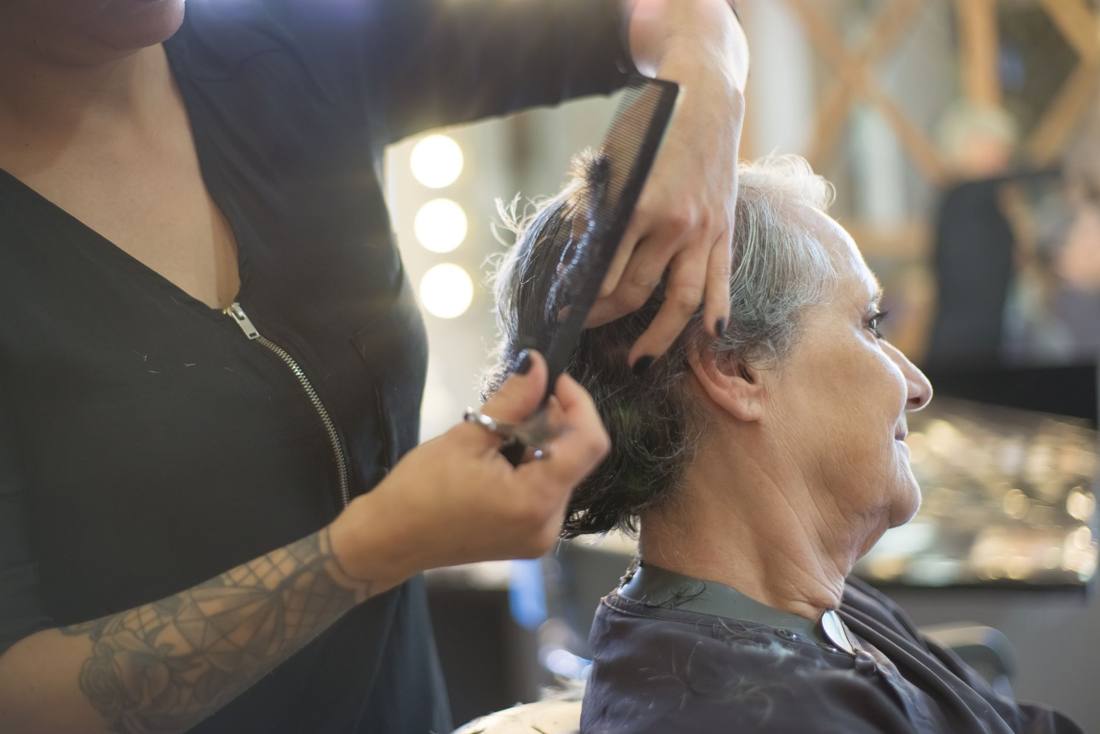 Hairdresser cutting senior woman's hair in a salon with close-up view of the hands and tools.