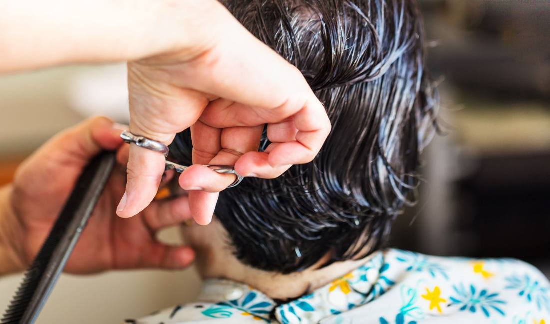 Close-up of a stylist cutting dark, wet hair in a salon setting, showcasing the precision and technique of hairstyling.
